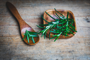 Branches and leaves of rosemary in a wooden bowl and on a wooden spoon