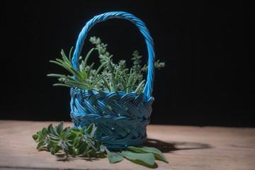 Branches of rosemary, oregano, sage and thyme in a little basket on a wooden surface