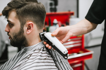 Closeup photo of a barber's hand with a haircut, creates a stylish hairstyle for a bearded man in a hair salon for men. Hairdresser cuts a client in a barbershop, close up