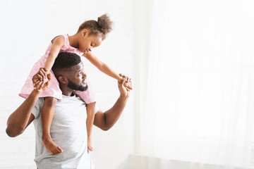 Black dad carrying little daughter on shoulders