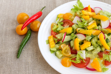 On a linen napkin lies a white plate with fresh vegetable salad for diet