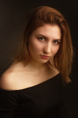 Naklejka premium Portrait in the photo Studio of brown-haired girl, on a black background in black clothes with open shoulders. Short hair.