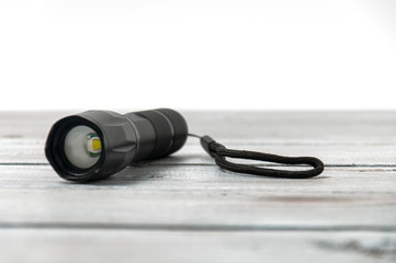 Small black pocket lamp on a gray wooden table on a white background. Turned off flashlight...