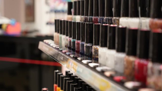 Rows of nail polish bottles in different colour and finish at cosmetic store, close up shot. Shallow depth of field, camera focused on middle, hand held shot