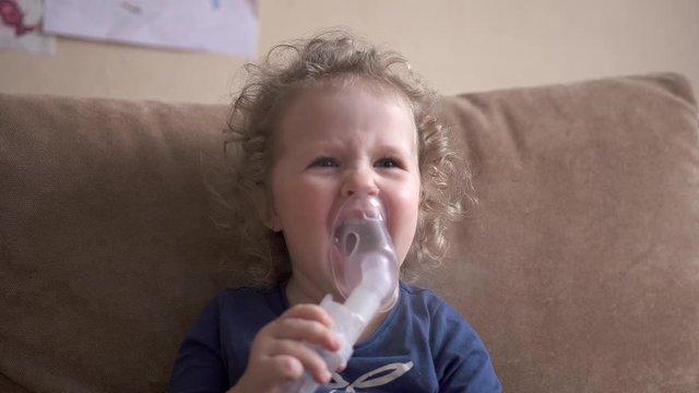 Happy funny child treats flu by inhaling inhalation vapor. Little girl treated with an inhalation mask on her face.