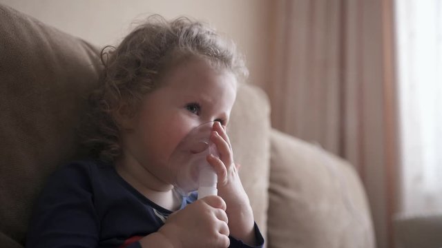 Happy funny child treats flu by inhaling inhalation vapor. Little girl treated with an inhalation mask on her face.