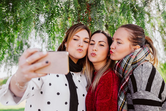 three girlfriends making a selfie by throwing a kiss in the park outdoors