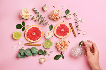 Top view of woman spraying perfume on pink background, flowers and citrus fruits representing aroma