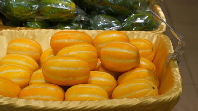 Ripe yellow oriental melon at stall of Korean supermarket, woman hand take one chamoe fruit. Popular product at Asia, small colorful striped plants stacked in container