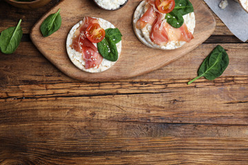 Puffed rice cakes with prosciutto, tomato and basil on wooden table, flat lay. Space for text