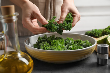 Woman cooking tasty kale salad on grey table, closeup