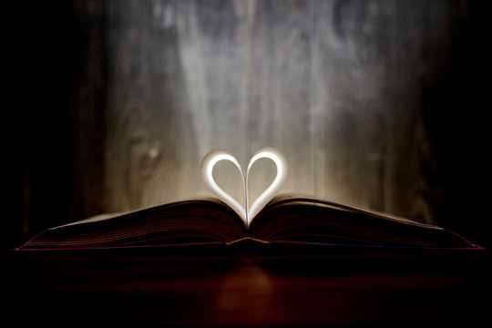 A heart from book pages shines in the dark.