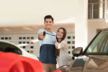 Happy couple with car key in modern auto dealership