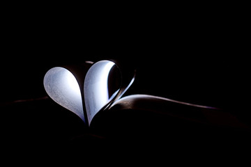 A heart from book pages shines in the dark.