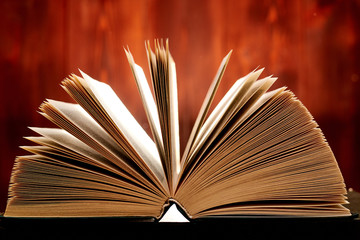 An opened thick book backlit by light on a brown background.