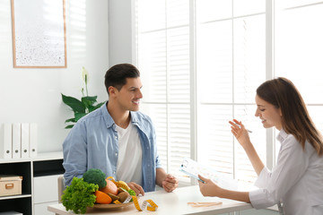 Young nutritionist consulting patient at table in clinic