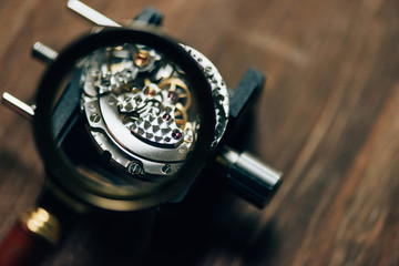 Selective focus of parts of mechanical wristwatch in magnifying glass on table