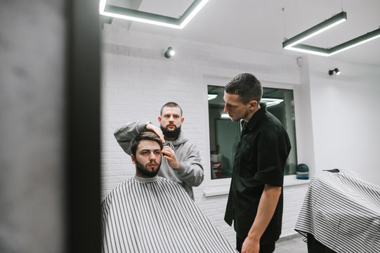 Two Barbers Create Hairstyle For Bearded Man In Bright Modern Hairdressing Salon. Male Model Cut 2 Hairdressers. Workshop On Male Haircuts In Barbershop, Training Barber Haircut