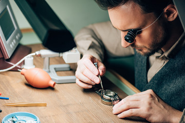 Side view of watchmaker in eyeglass loupe working with wristwatch by equipment on table