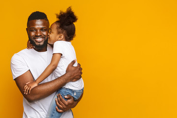 Preschool black girl kissing smiling father over yellow background - obrazy, fototapety, plakaty