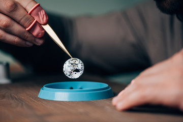 Cropped view of watchmaker holding watch part above tool tray on table
