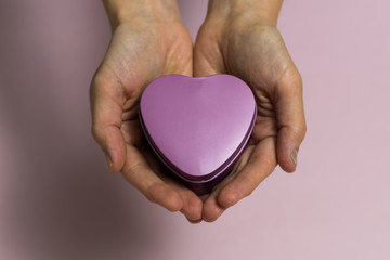 Obraz premium In female young hands lies a small heart-shaped box, close-up, on a light pinkish background.