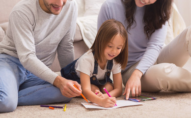 Loving parents teaching their little daughter drawing, sitting together on floor