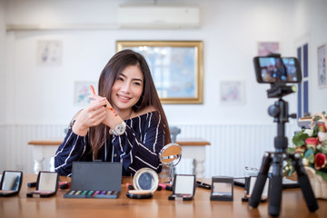 Young asian woman blogger with makeup cosmetics recording video clip online by smartphone at home.