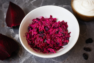 A light simple salad of beets and raisins with sour cream on a dark gray marble background. Around - the ingredients. The concept of simple homemade food, healthy eating.