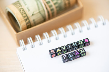 Words savings plan laid out from blocks with letters, money banknotes dollars in craft box on table