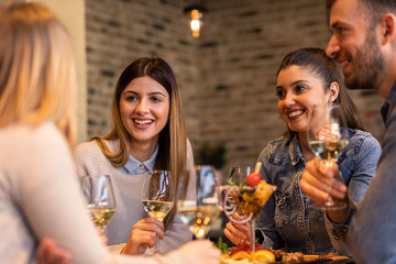 Group of young friends having fun in restaurant, talking and laughing while dining at table.	