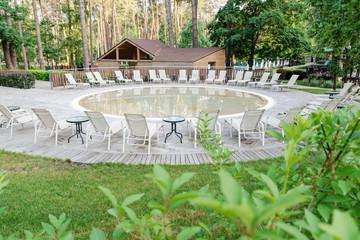 An open-air round artificial pond. Sun beds and tables for rest near the round pool. Relax and spa concept
