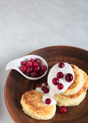 Fresh cottage cheese pancakes are stacked on top of each other and watered with sour cream and frozen cranberries.