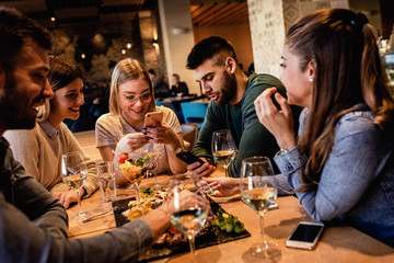 Group of young friends having fun in restaurant, talking and laughing while dining at table.	
