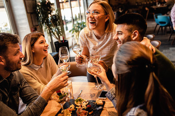 Group of young friends having fun in restaurant, talking and laughing while dining at table.	