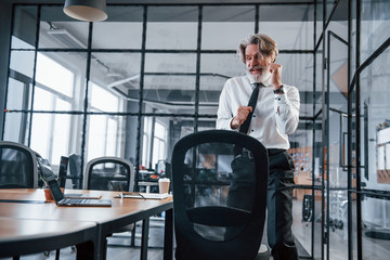 Happy dancing mature businessman with grey hair and beard in formal clothes celebrating success in the office
