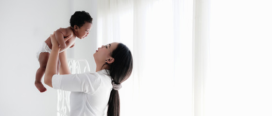 diversity of asian mother holding her mixed race black baby boy african american and asian in white...