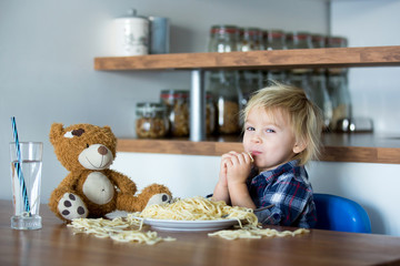 Little baby boy, toddler child, eating spaghetti for lunch and making feeding teddy bear friend