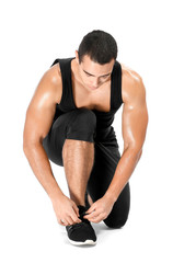 Sporty African-American man tying shoelaces on white background