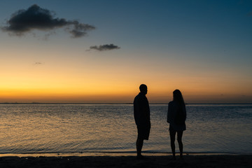Silhouettes of a adult couple on the beach on a summer sunset background  