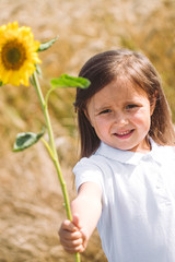 Happy little girl smelling a sunflower on the field .