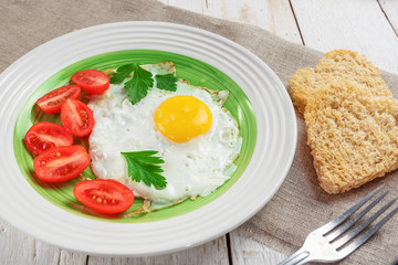 Fried eggs, heart shaped bread and red tomatoes on linen napkin on wooden background