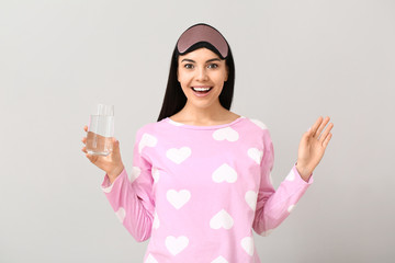 Beautiful young woman with glass of water on light background