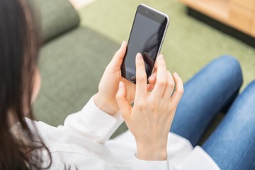ソファに座ってスマートフォンを操作する女性