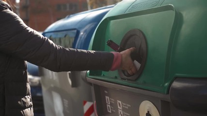 Woman's hand putting a glass bottle into a recycling bin street barcelona spain