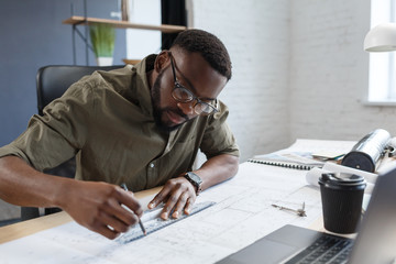 Afro-American architect working in office with blueprints.Engineer inspect architectural plan,...