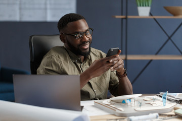 Young Afro-American man using smartphone and smiling. Happy businessman using mobile phone apps, texting message, browsing internet, looking at smartphone. Young people working with mobile devices.
