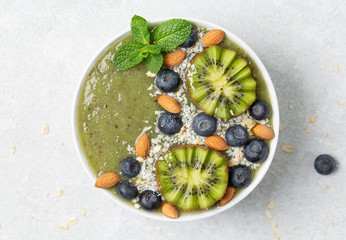 Healthy Green Smoothie in the Bowl from banana and spinach with blueberries, mint, granola, almond, coconut and kiwi. Breakfast smoothie bowl. 