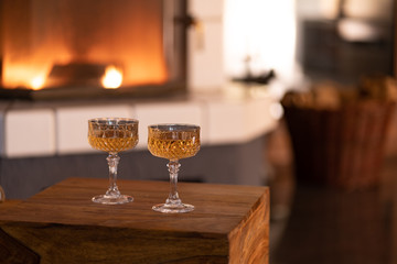 candle in a glass and two wine glasses on a wooden box, romantic candlelight against a blurred background with a fireplace, wood basket