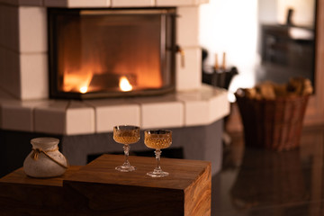 glass vase and two wine glasses on a wooden box, romantic candlelight against a blurred background with a fireplace, wood basket